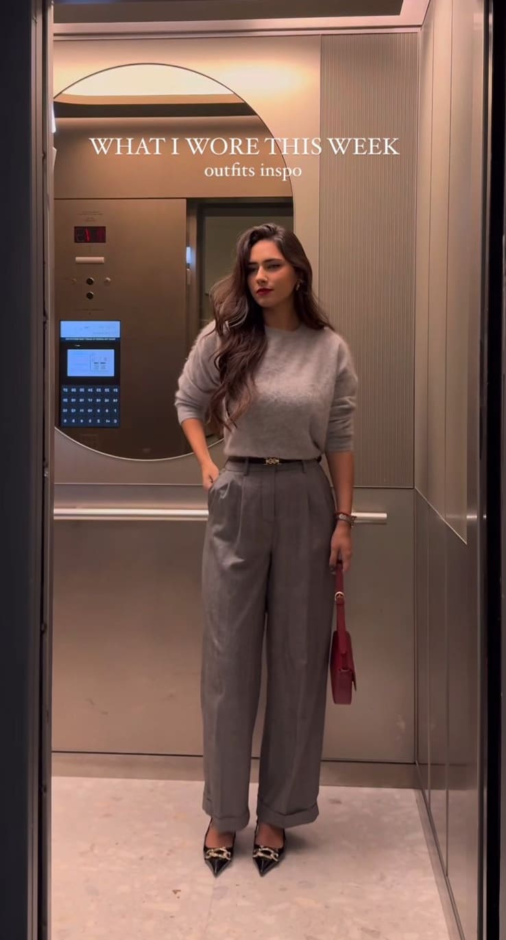 Soft grey crewneck sweater with grey pleated trousers and a red shoulder bag